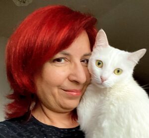 Kiran Kaur Saini, with bright red hair, with her white cat, Minka.